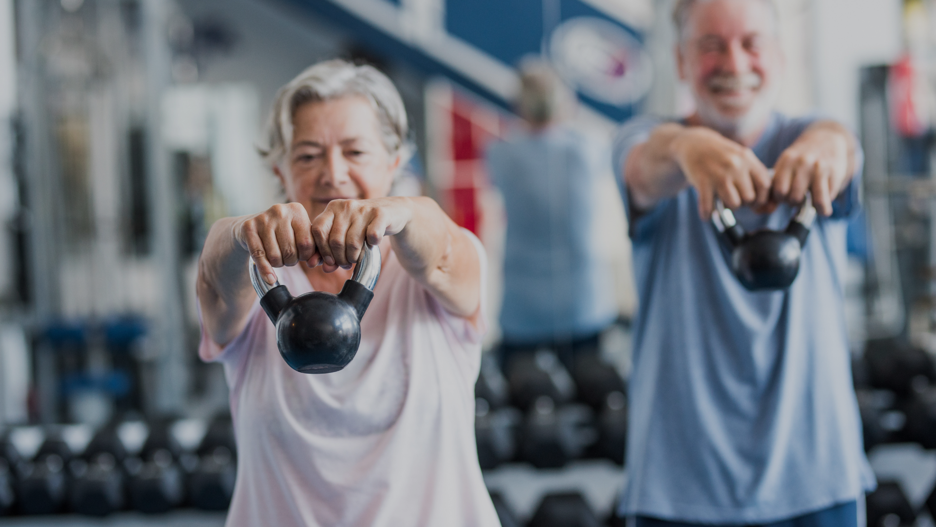 A man and a woman are lifting kettlebells in a gym.