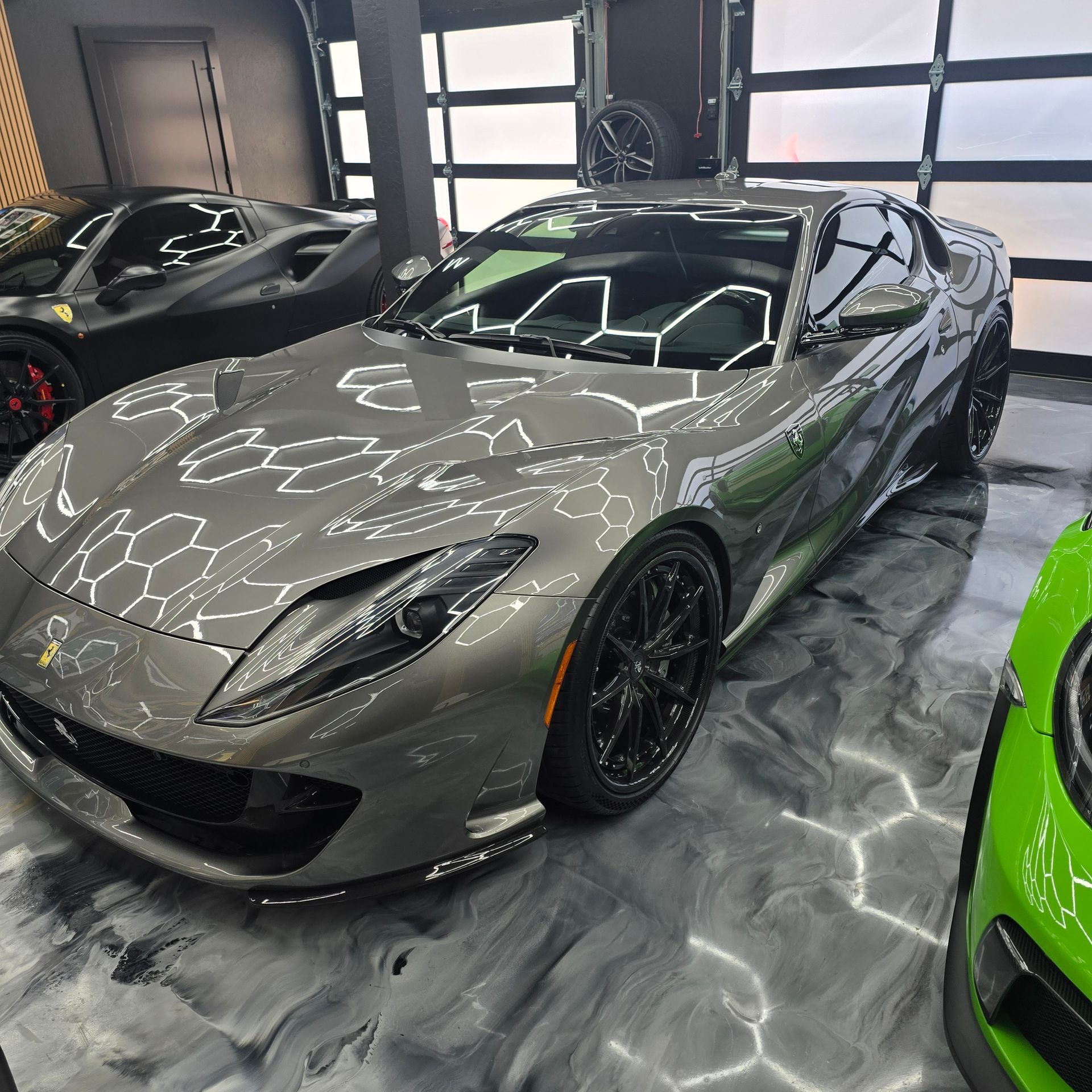 Gray sports car in a showroom, with a green car partially visible beside it.