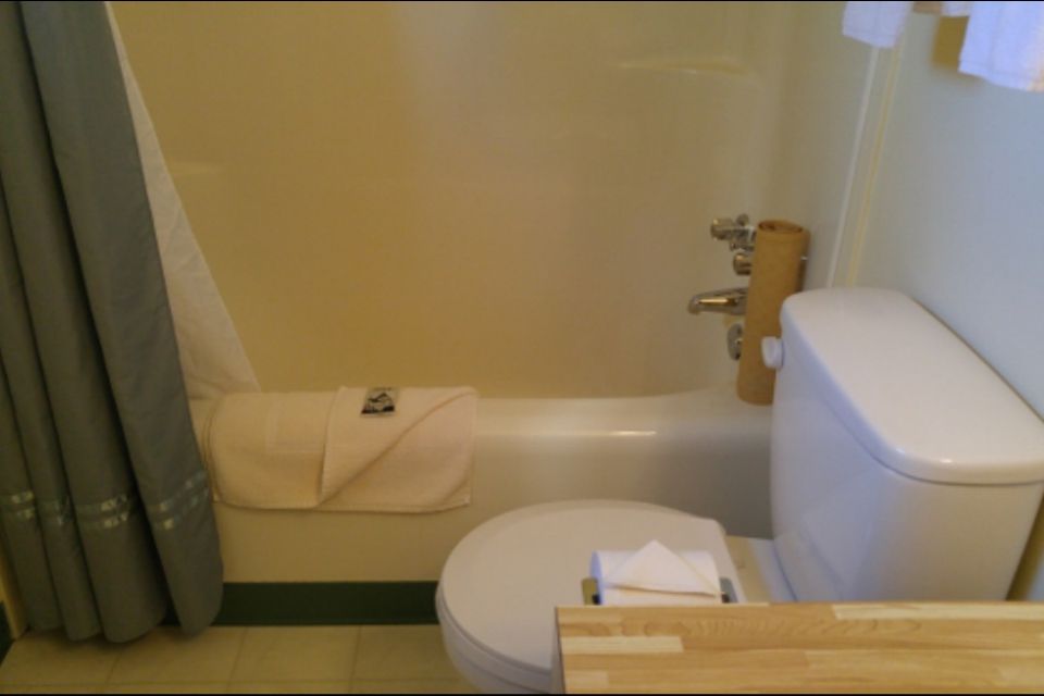 A small bathroom with a toilet and bathtub. Beige walls, gray shower curtain, and a folded towel on the tub.