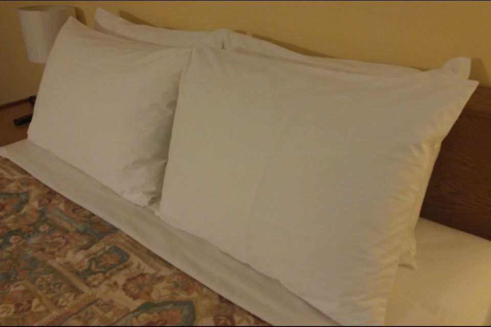 Two white pillows on a bed with a patterned bedspread and wooden headboard.