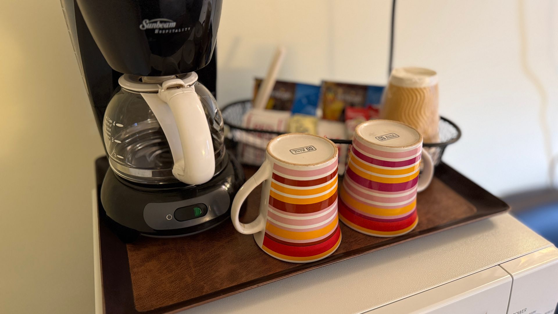 Coffee maker with mugs and supplies on a tray, indoors.