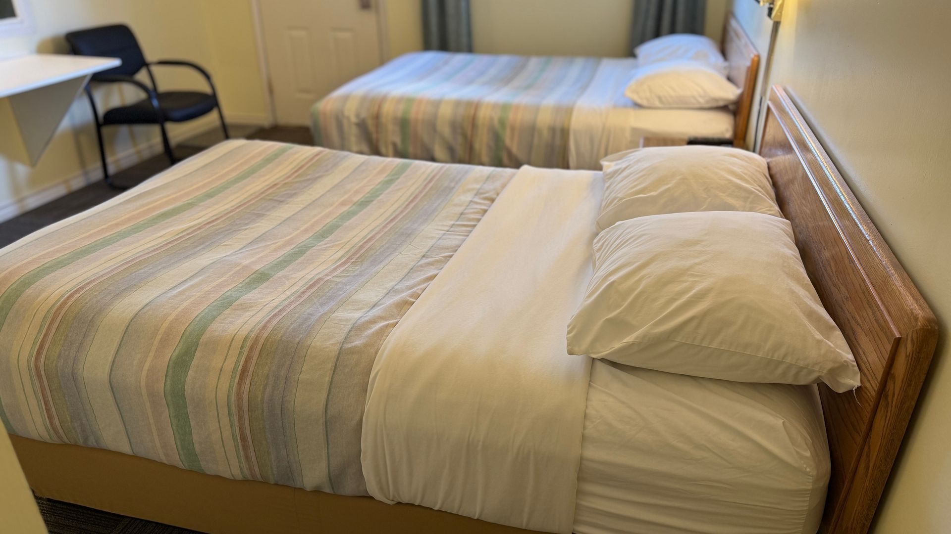 Two beds in a motel room with striped bedspreads, white linens, and a desk in the corner.