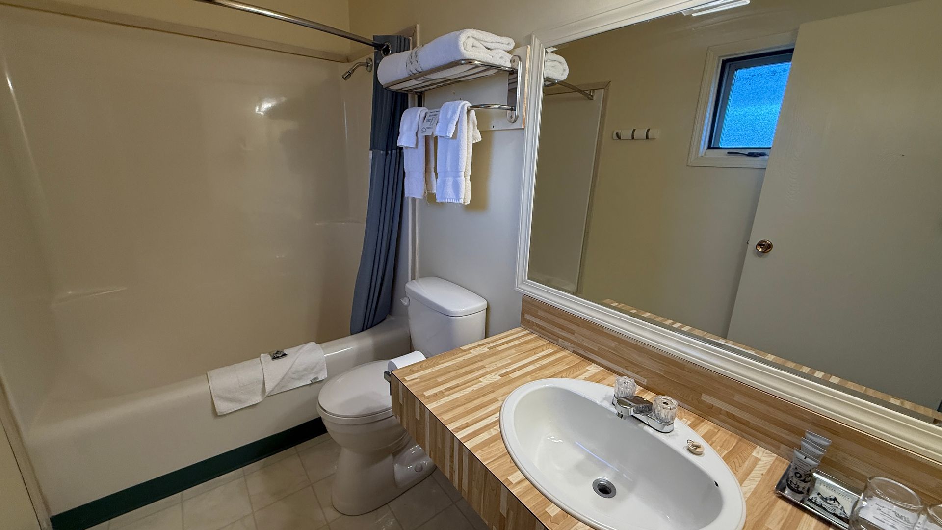 Bathroom with tub, toilet, and sink. Towels on a rack. Mirror above the sink. Blue shower curtain.