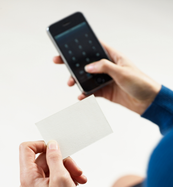 Hand holding a blank card near a smartphone on a keypad screen