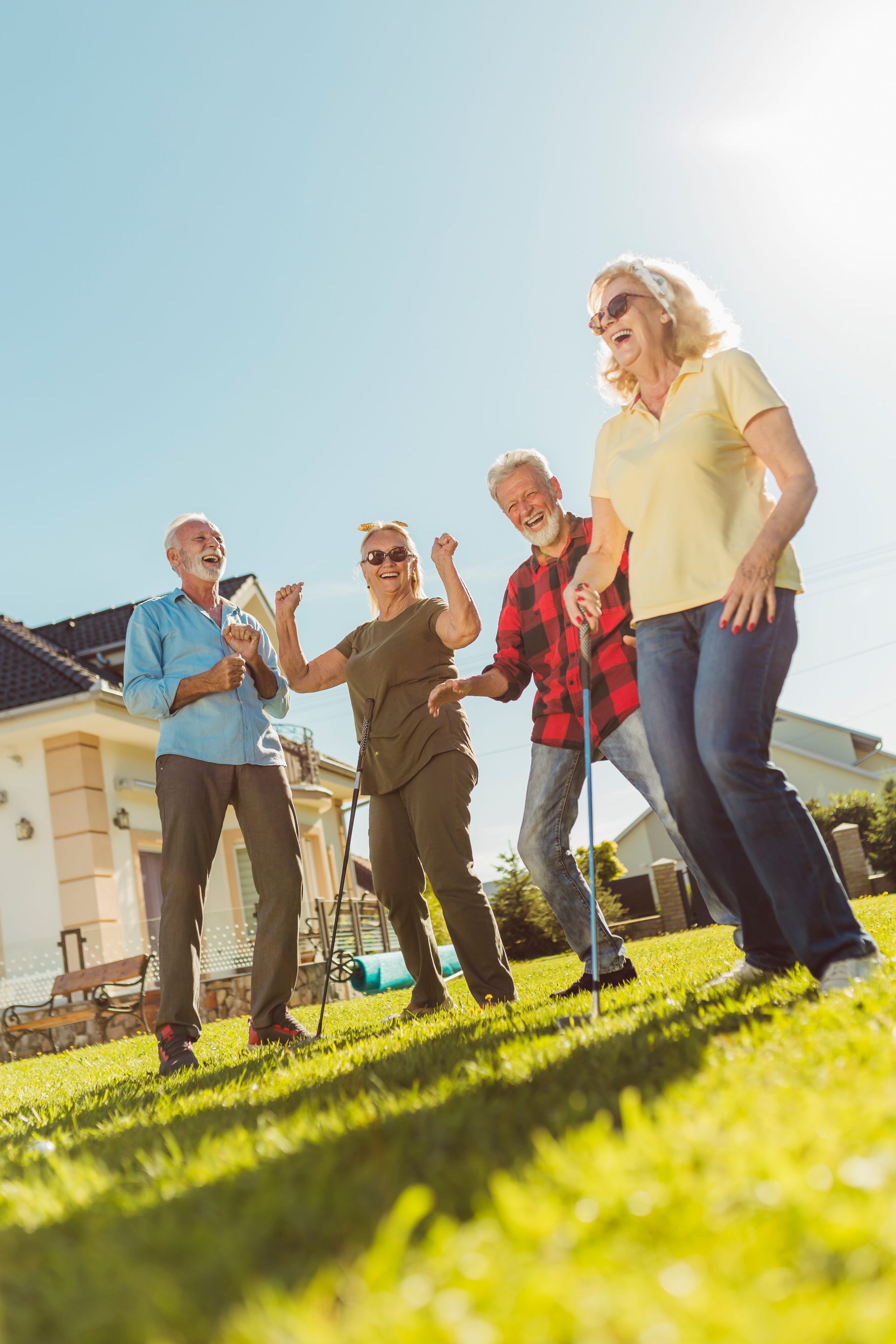 Four friends dancing and laughing on a sunny lawn outside a house