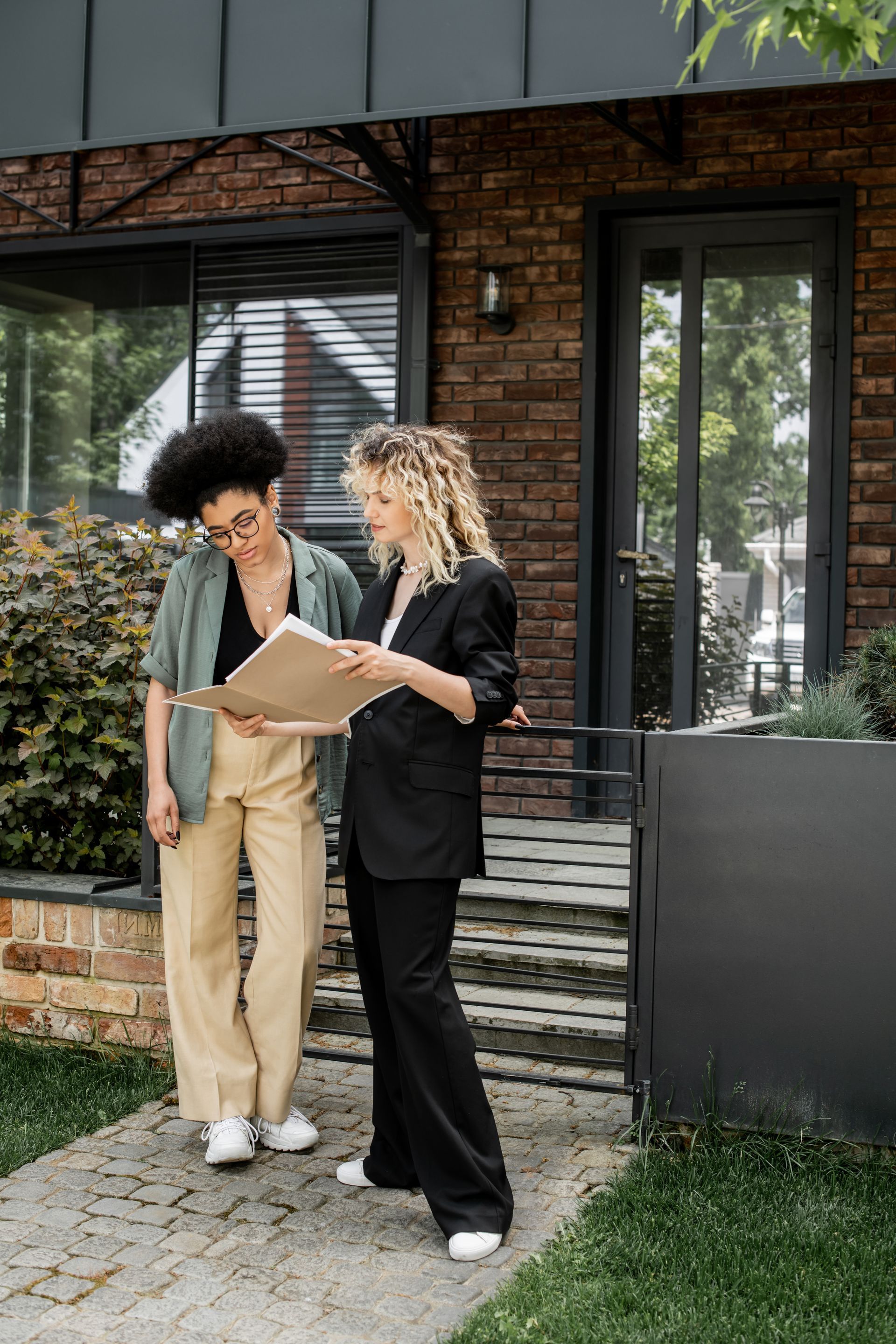Two people reviewing a clipboard outside a brick building with large windows.