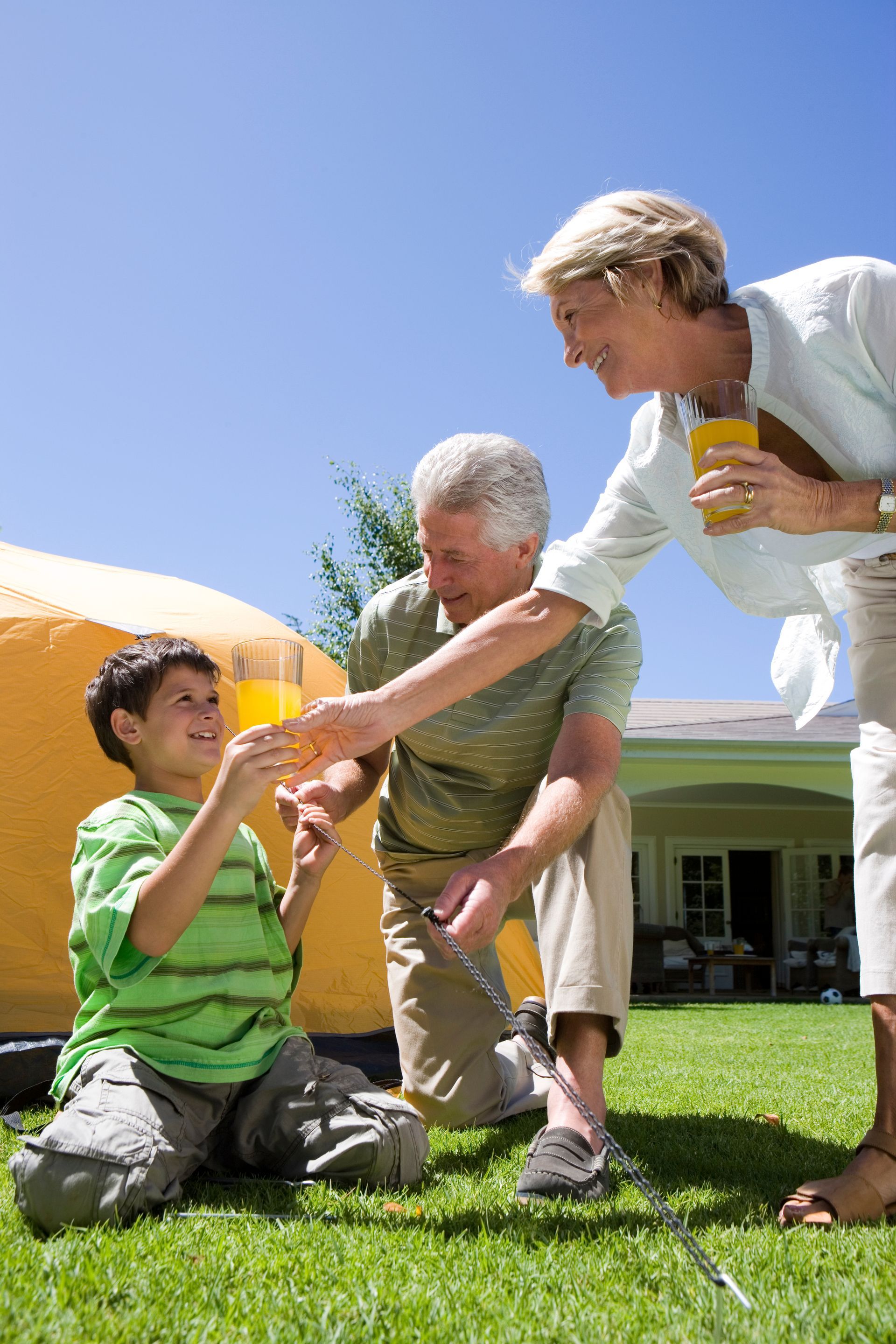 Two adults and a child sharing juice outdoors on a sunny lawn