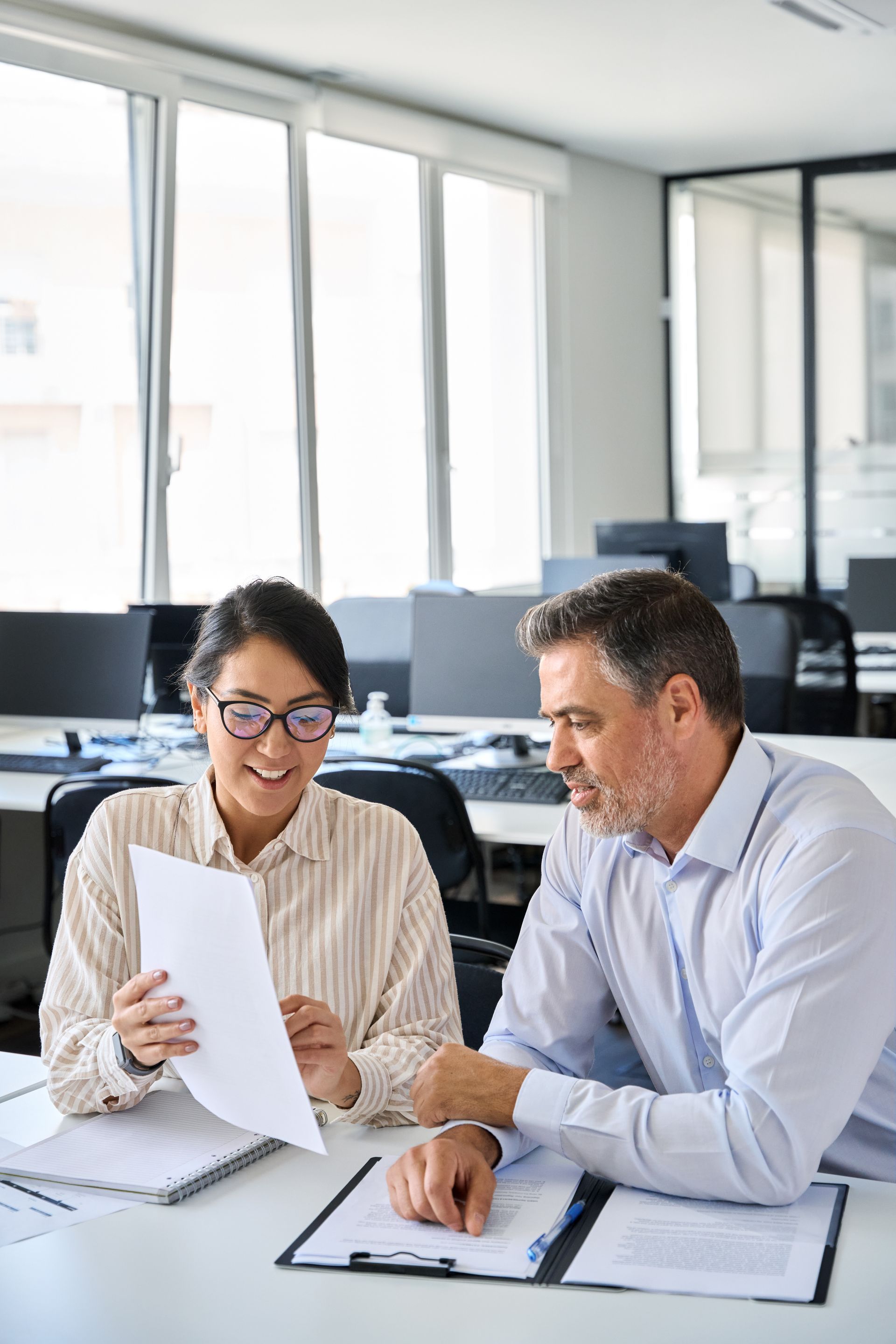 Two coworkers reviewing documents at a desk in a bright office