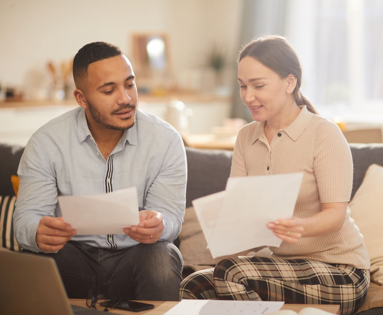 Two people sitting on a couch, reviewing papers in a bright living room.
