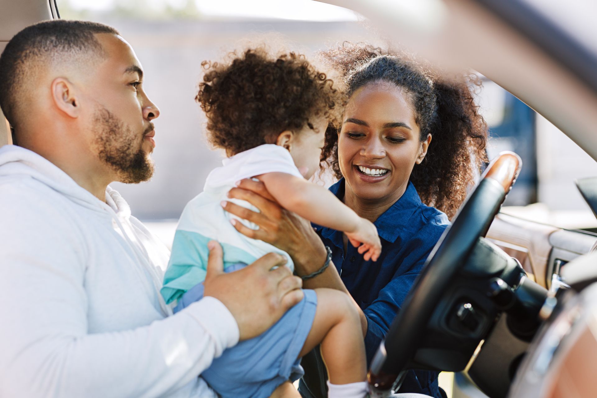 Adult holding a toddler in a car, smiling and adjusting the child in the back seat