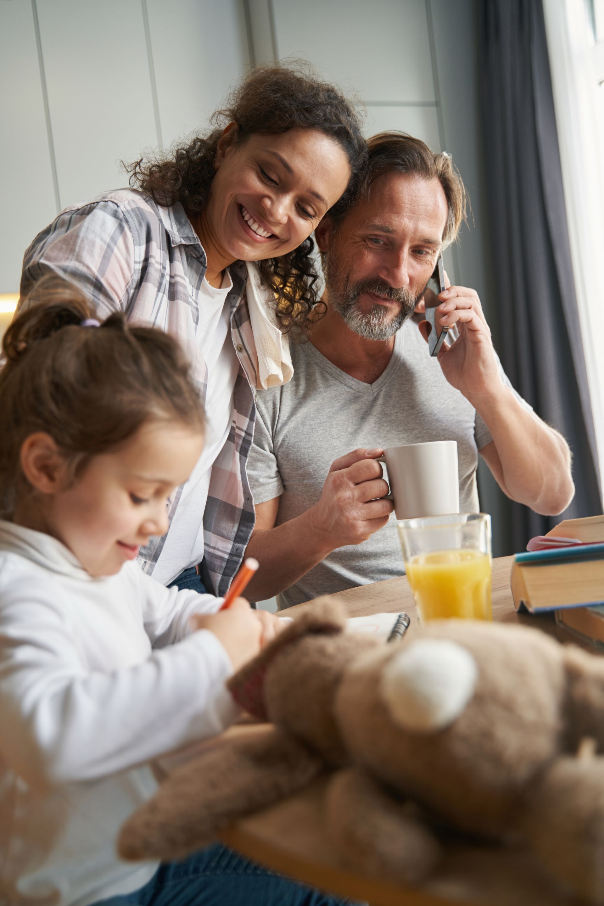 Family sharing breakfast at a table, smiling and chatting near a window.