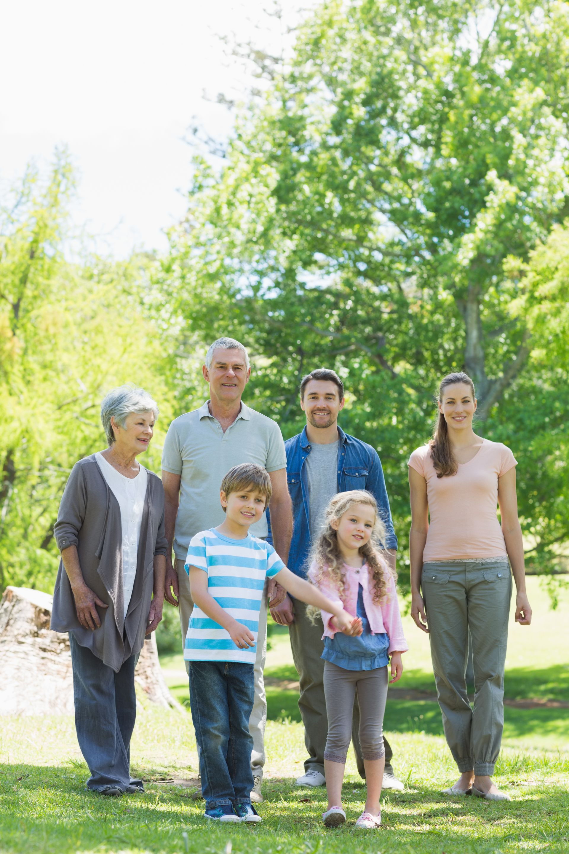 Group of six people standing outdoors in a sunny green park, smiling at the camera.
