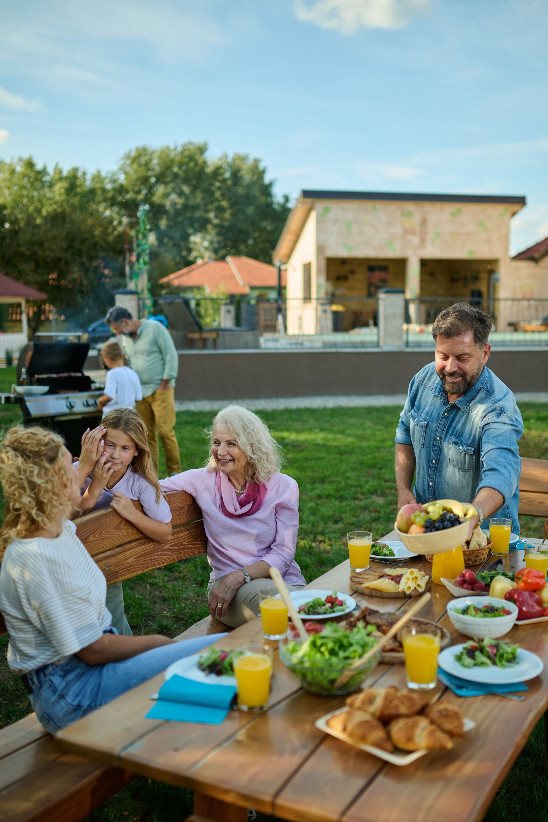 People enjoying an outdoor meal at a picnic table in a backyard garden