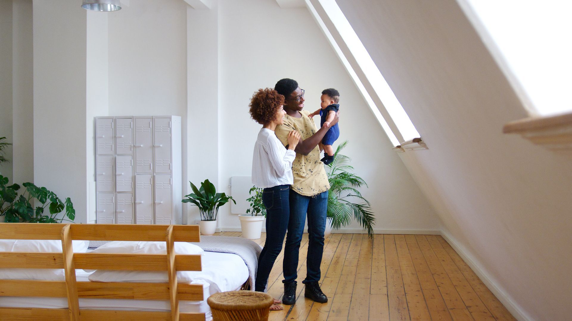 Couple standing in a bright room, holding a baby near a large slanted window