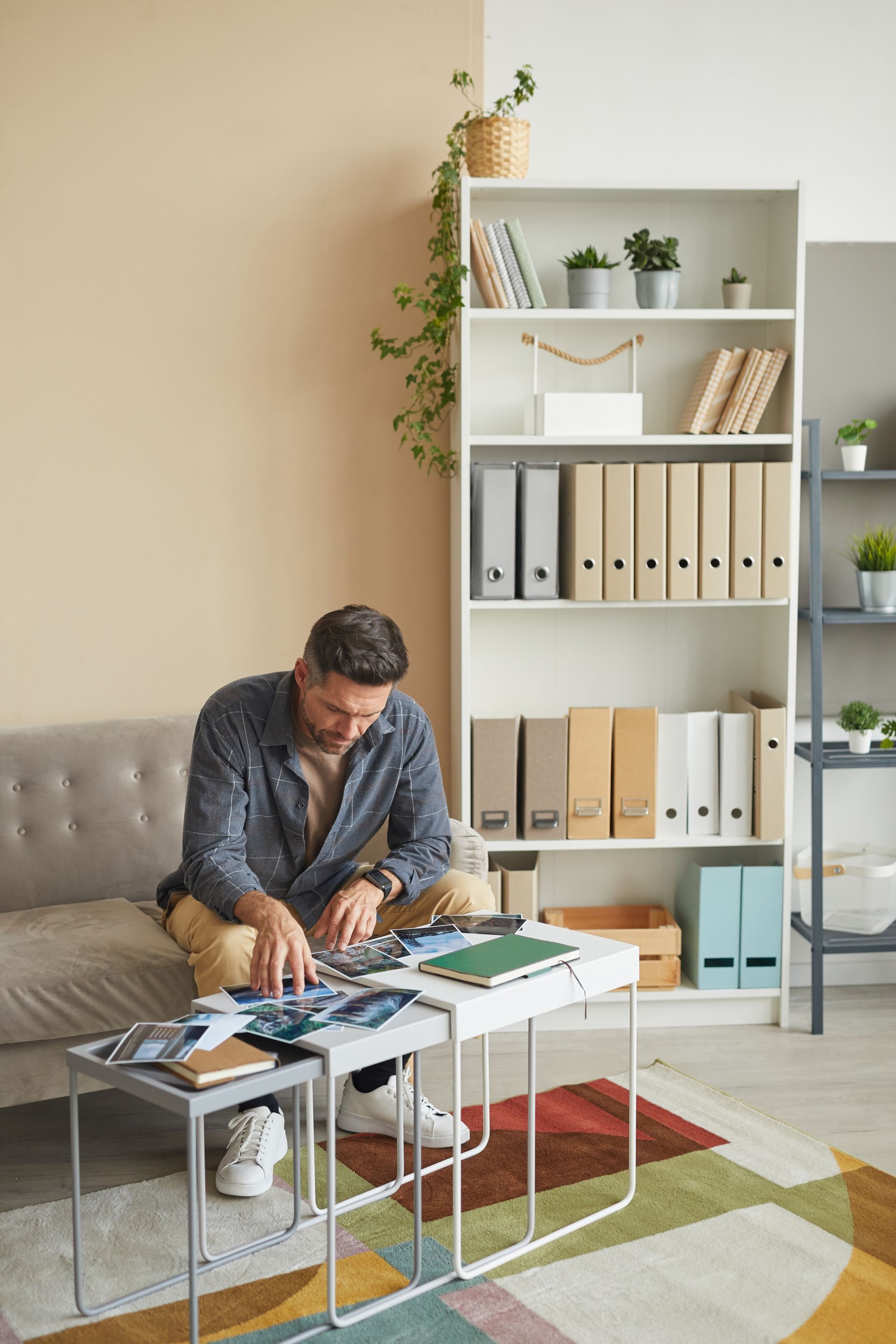 Person sorting papers at a coffee table in a bright living room with shelves and a gray sofa