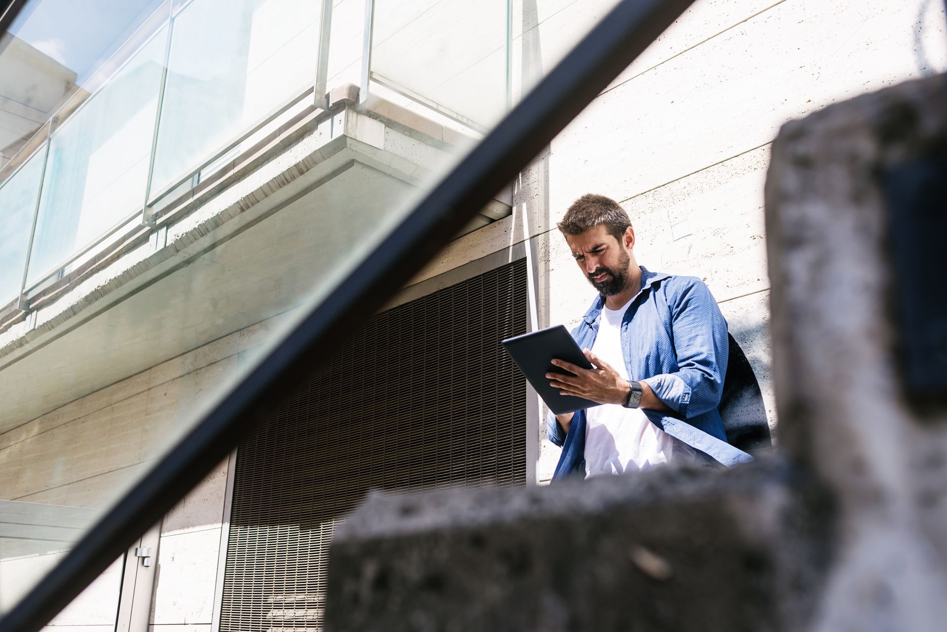 Man in a blue shirt reviewing a clipboard outside a building, seen through diagonal railings