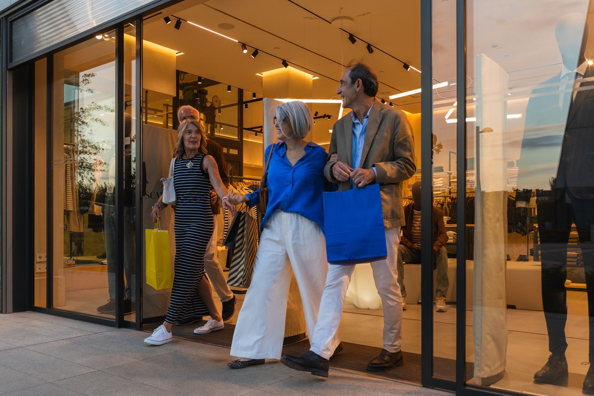 Three friends walking out of a glass storefront at sunset, smiling and chatting.
