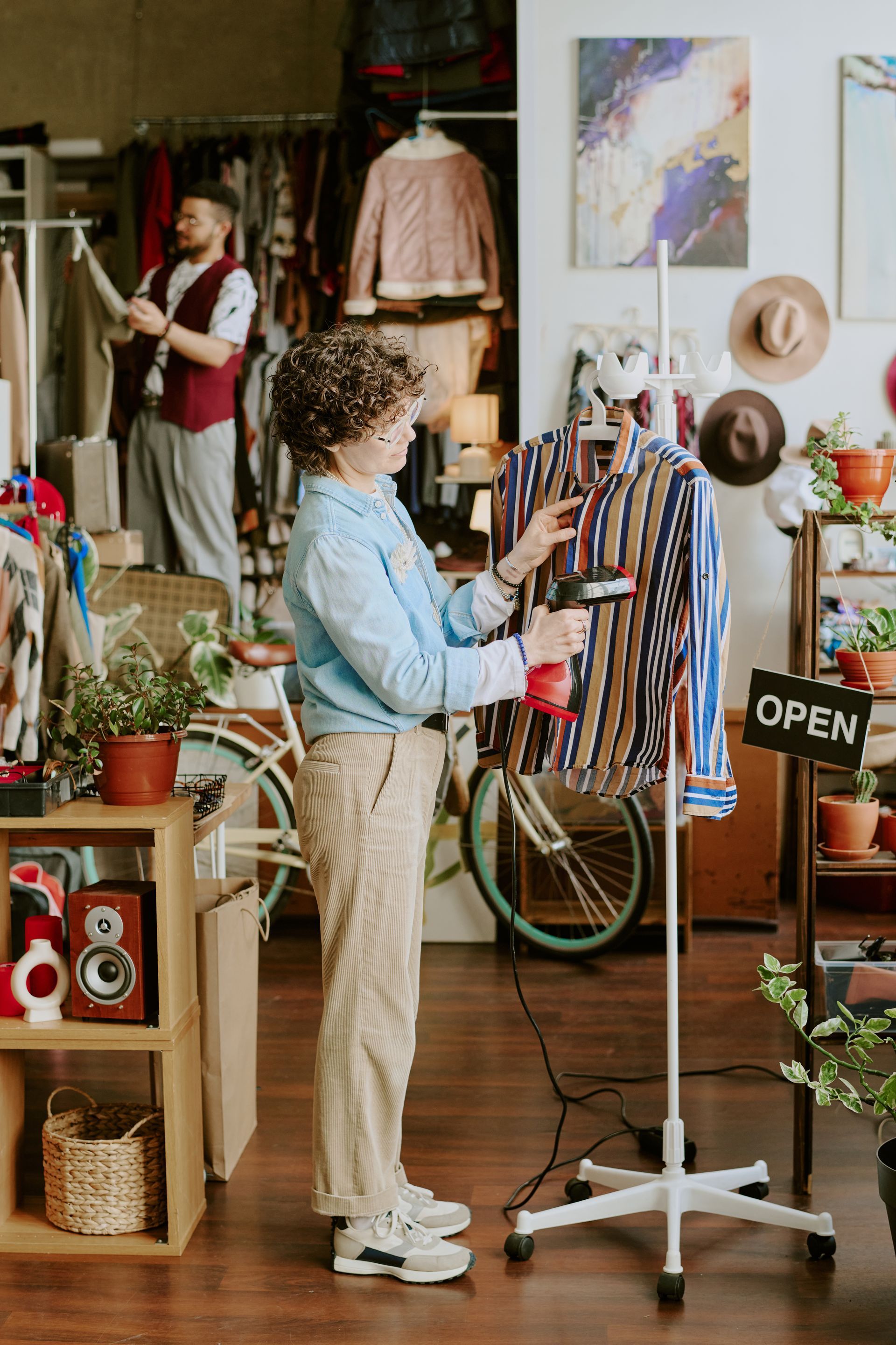 Person arranging clothes on a rack in a cozy vintage shop with plants and decor