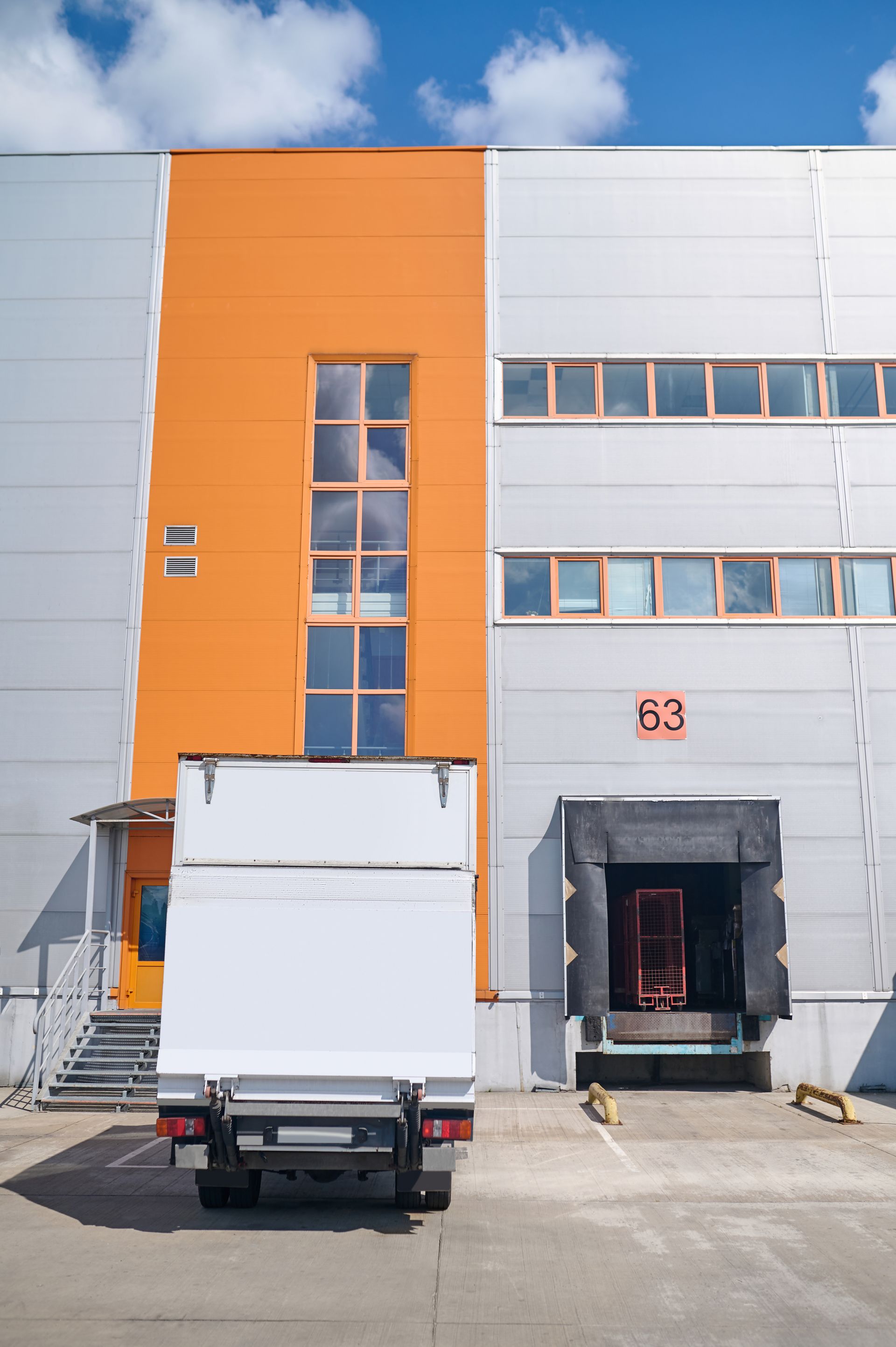 Truck parked outside a gray and orange industrial building with the number 63 above the entrance.
