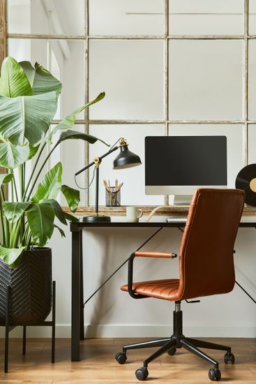 Modern home office with desk, computer monitor, lamp, orange chair, and large green plant