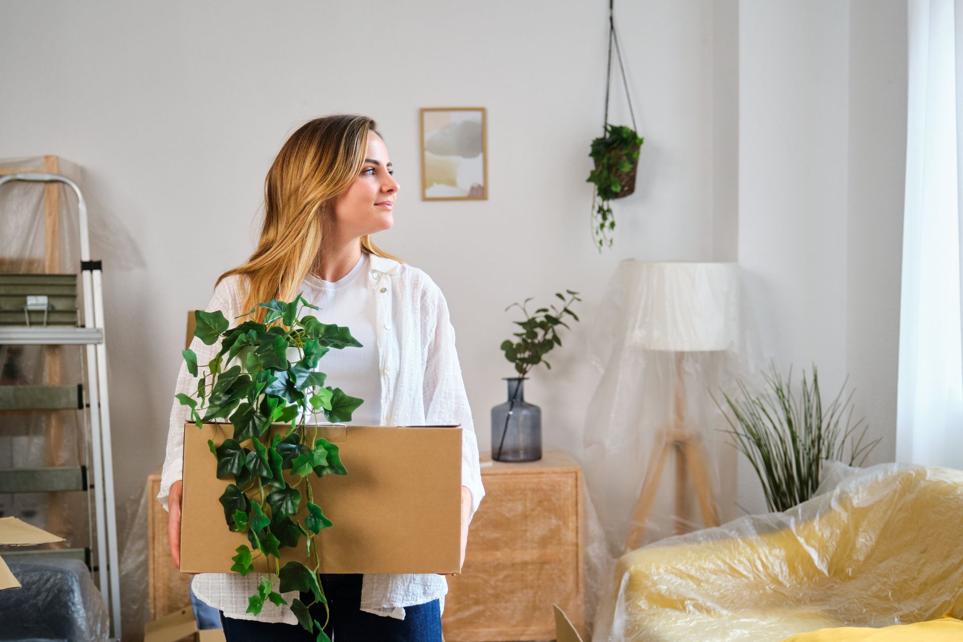 Woman carrying a box of houseplants in a bright living room