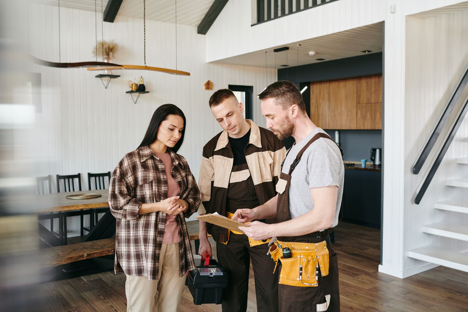 Three people in a bright office review plans together, with one holding a clipboard.