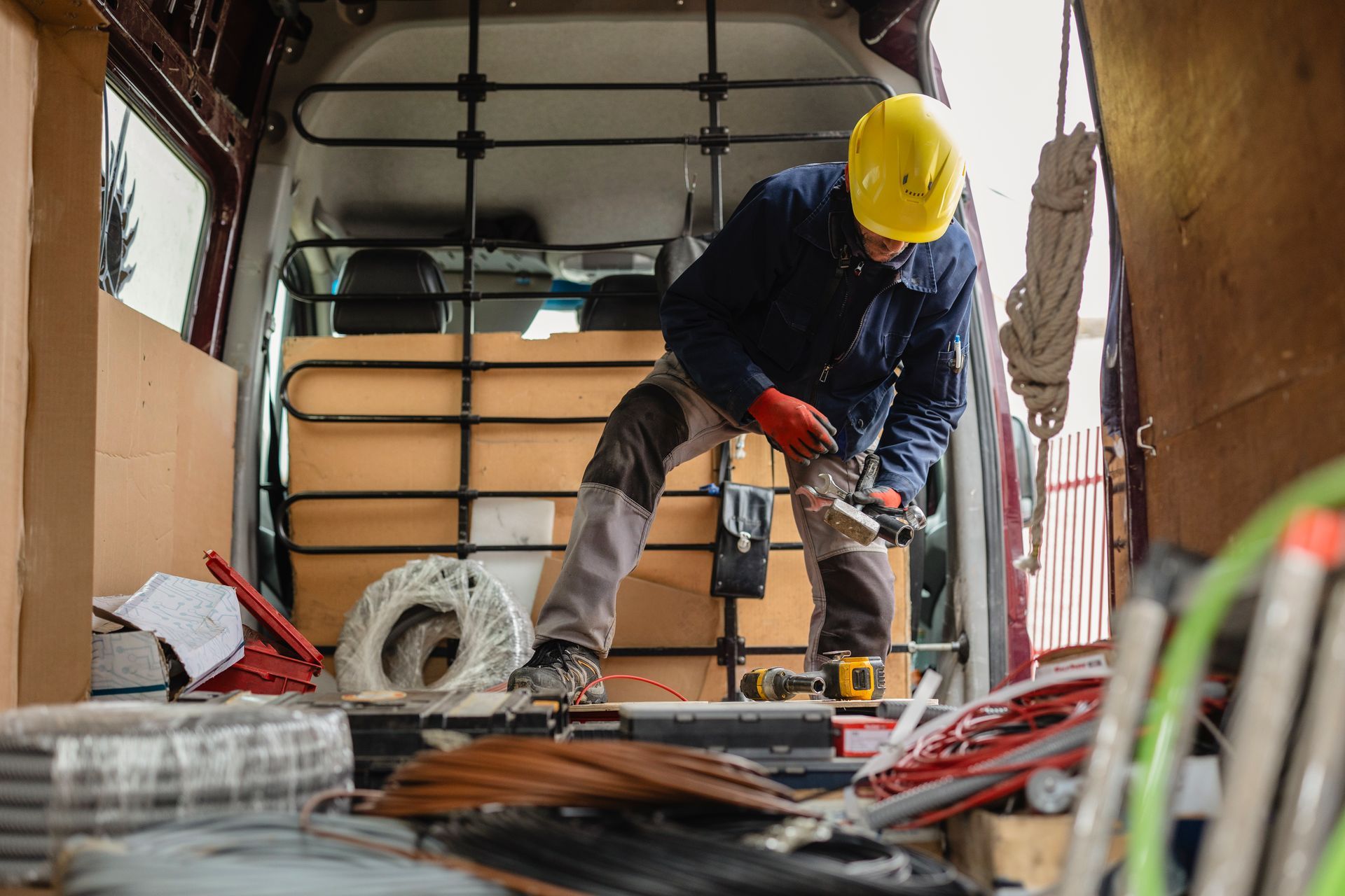 Construction worker in a yellow hard hat drilling on a floor inside a work van or trailer