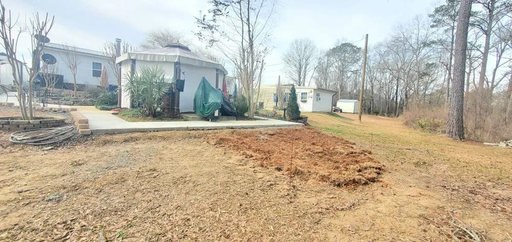 Dirt and grass lead to white buildings and trees on a cloudy day.