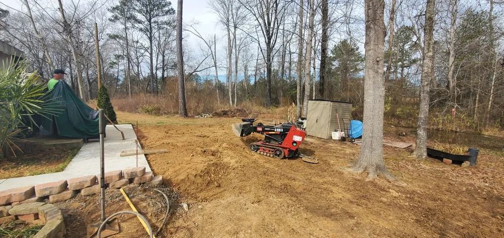 A wooded lot with dirt and a small red machine. Trees in the background, a path, and a covered object.
