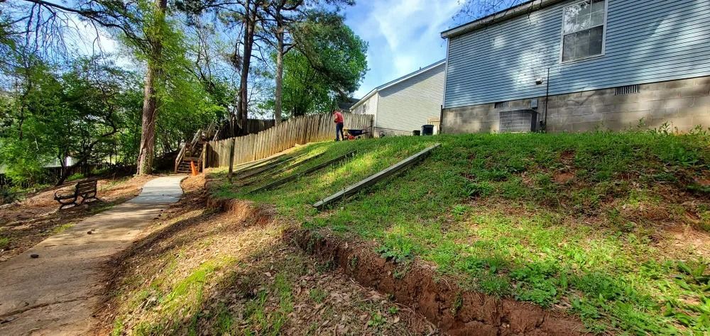 A path leads to a grassy hill with a building on top. A person stands near a wooden fence.