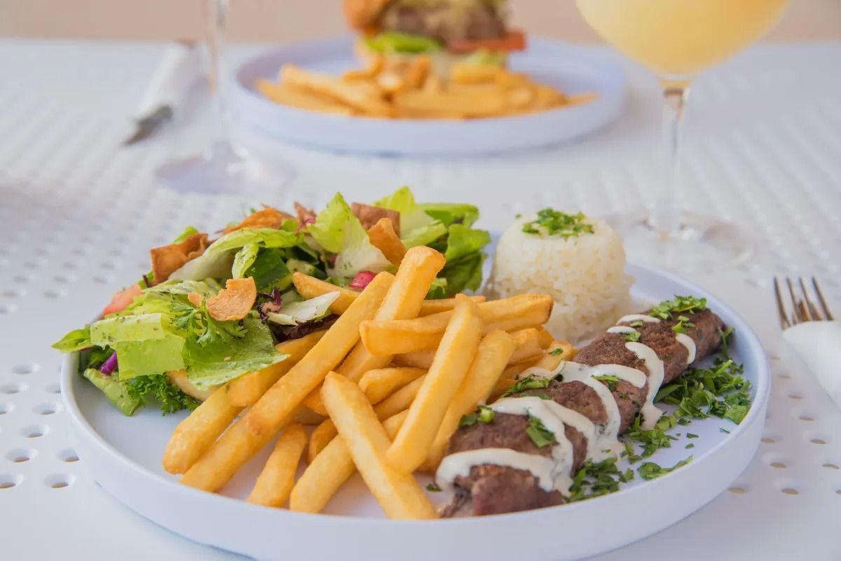 A plate featuring a meat skewer with sauce, French fries, a green salad, and a scoop of rice on a table.