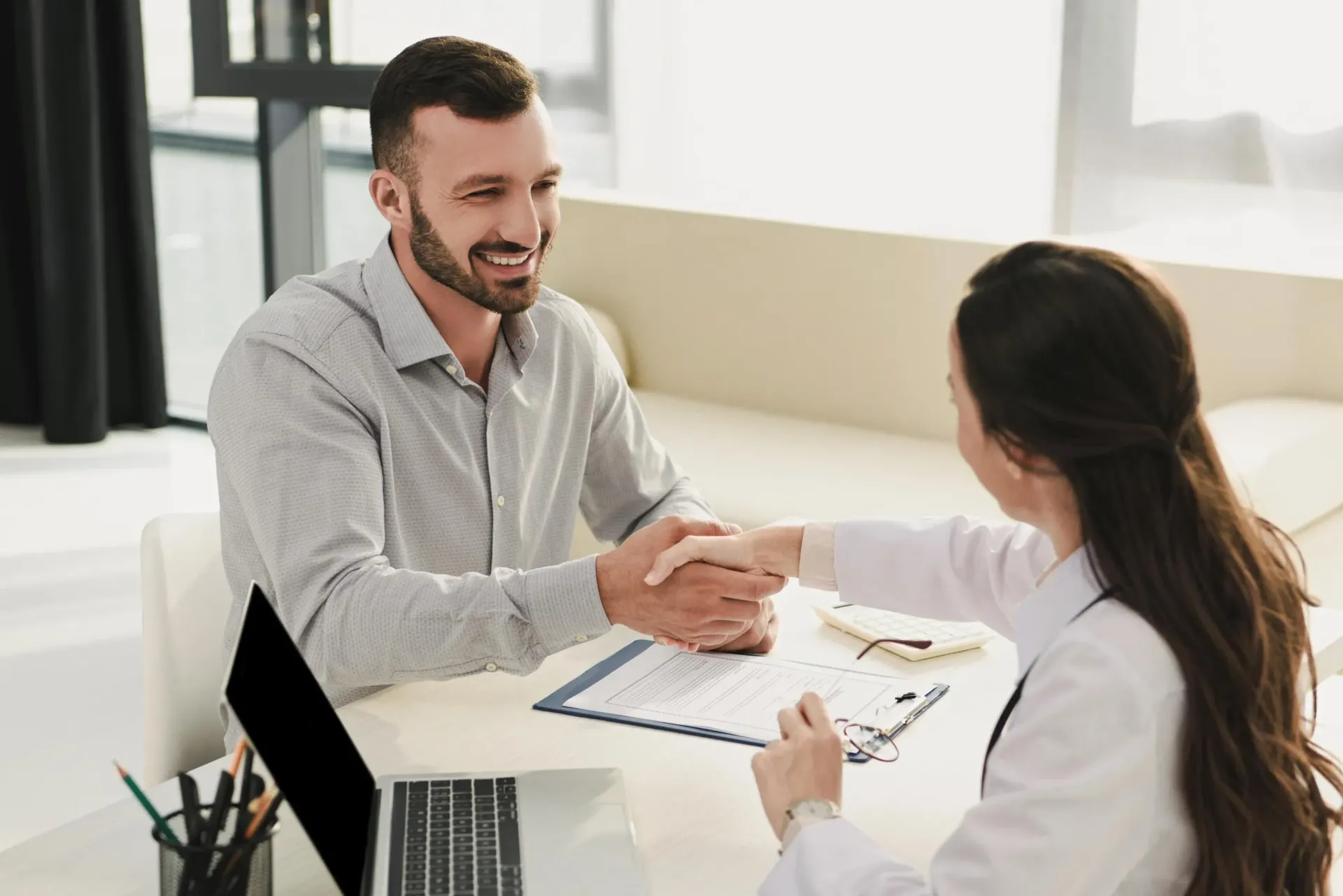 A man and a woman are shaking hands while sitting at a table.