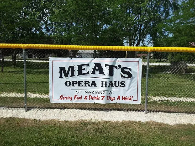 A sign for meat 's opera haus is hanging on a fence