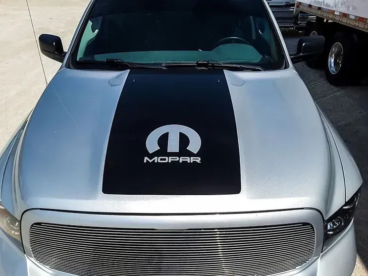 A silver mopar truck with a black hood stripe
