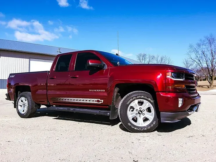 A red truck is parked on a dirt road in front of a building.
