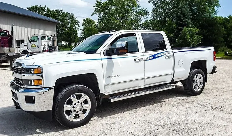 A white truck is parked in a gravel lot in front of a building.