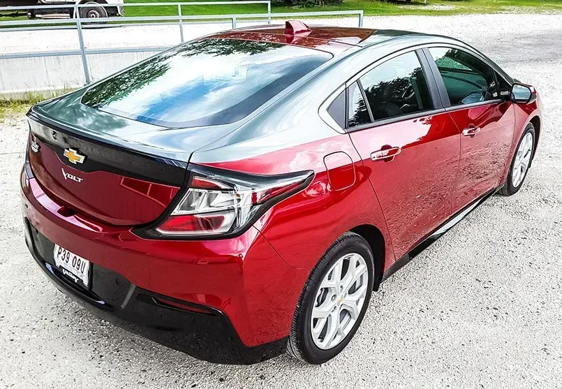 A red chevrolet volt is parked in a gravel lot.