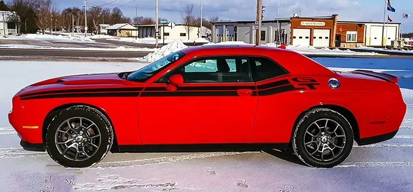 A red dodge challenger is parked in the snow