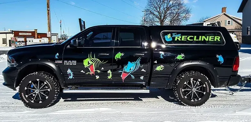 A black truck with a recliner canopy is parked in the snow.