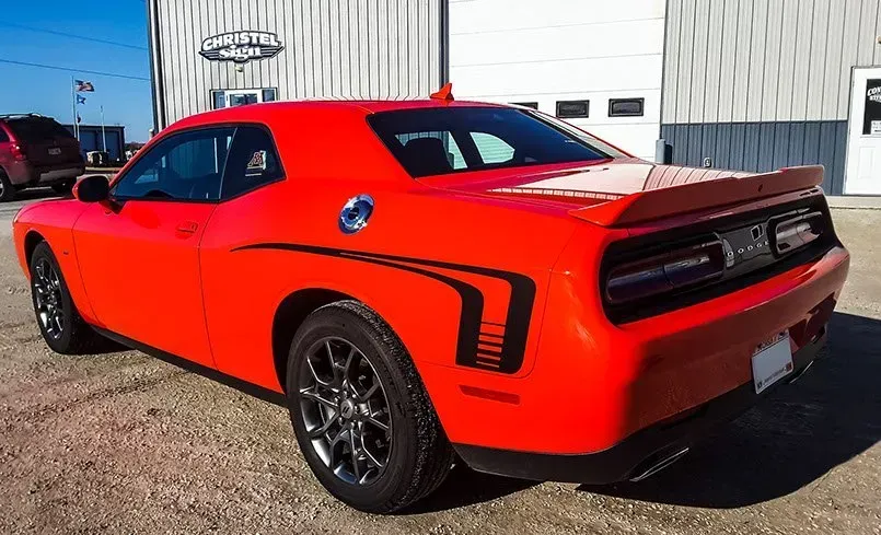 A red dodge challenger is parked in front of a building.