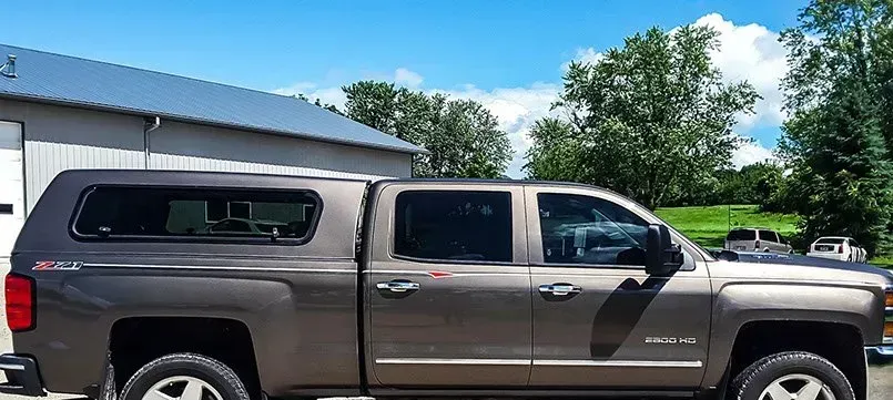 A truck with a canopy on top of it is parked in front of a building.