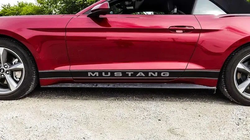 A red mustang is parked on the side of the road.
