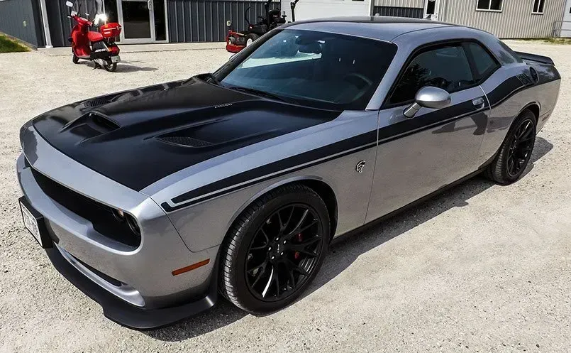 A silver and black dodge challenger is parked in a gravel lot.
