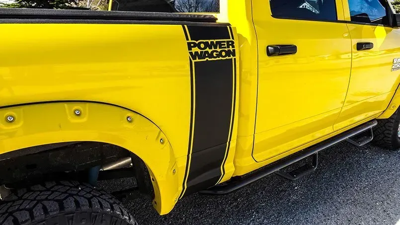 A yellow truck with a black stripe on the side is parked on the side of the road.
