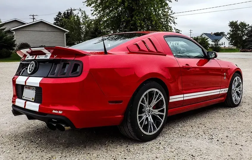 A red ford mustang is parked in a gravel lot