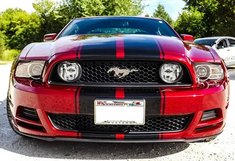 A red mustang with black stripes is parked in a parking lot.