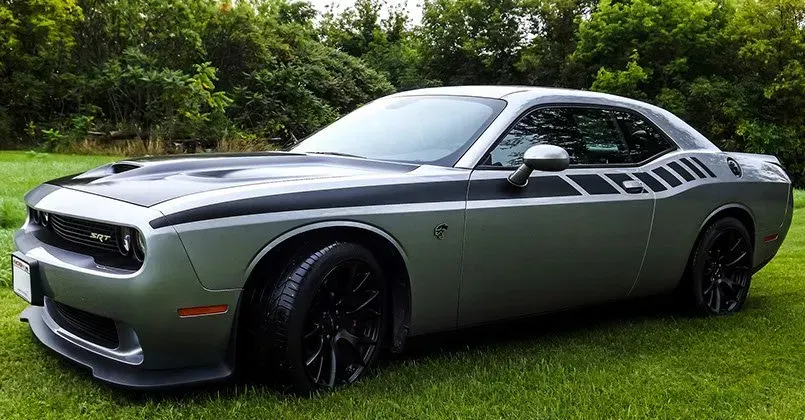 A silver dodge challenger is parked in a grassy field.