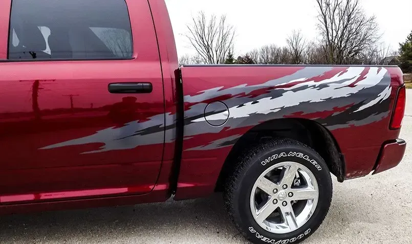 A red dodge ram truck with a camouflage design on the side is parked on the side of the road.