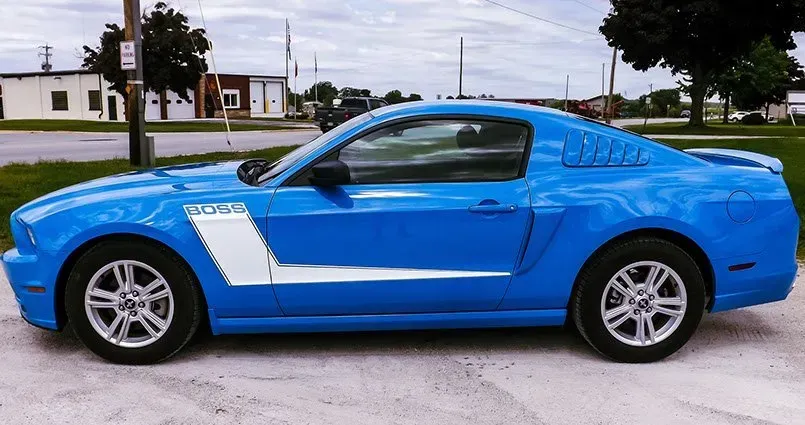 A blue mustang is parked on the side of the road.