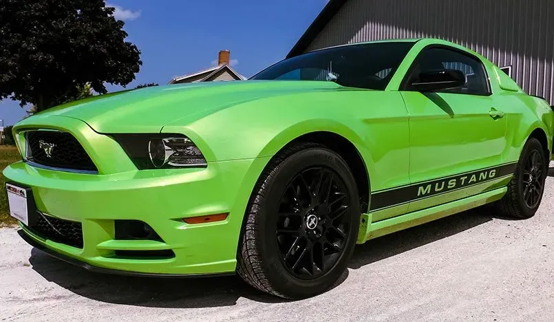 A green mustang is parked in front of a building.